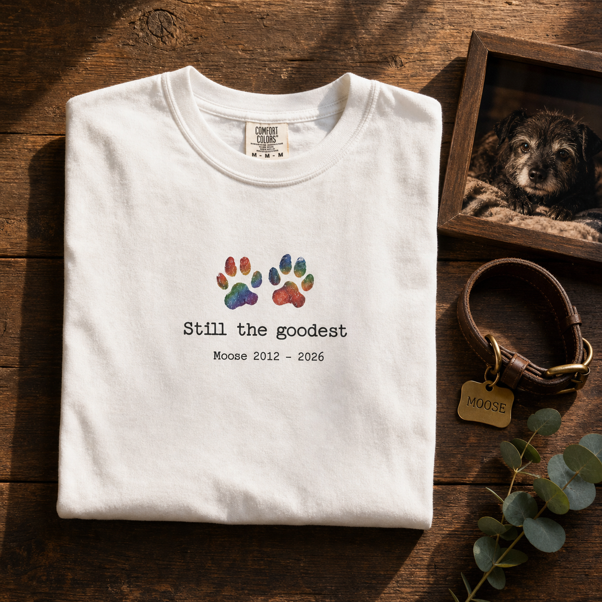 Still The Goodest personalized memorial tee beside a framed photo of the dog